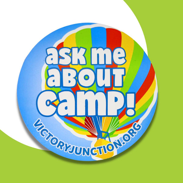 5 x 5 indoor/ outdoor circle magnet. The magnet features a bold, white text overlay that reads "ask me about camp!" The text is situated on a light blue background, with a red, yellow, green and blue hot air balloon. With the same text, "ask me about camp!"  which appears in the center of the image. Also displaying "VICTORYJUNCTION.ORG" below the hot air balloon.. 