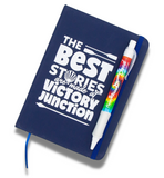 A tie-dye pen sitting on top of a journal that reads "The Best Stories are made at Victory Junction."